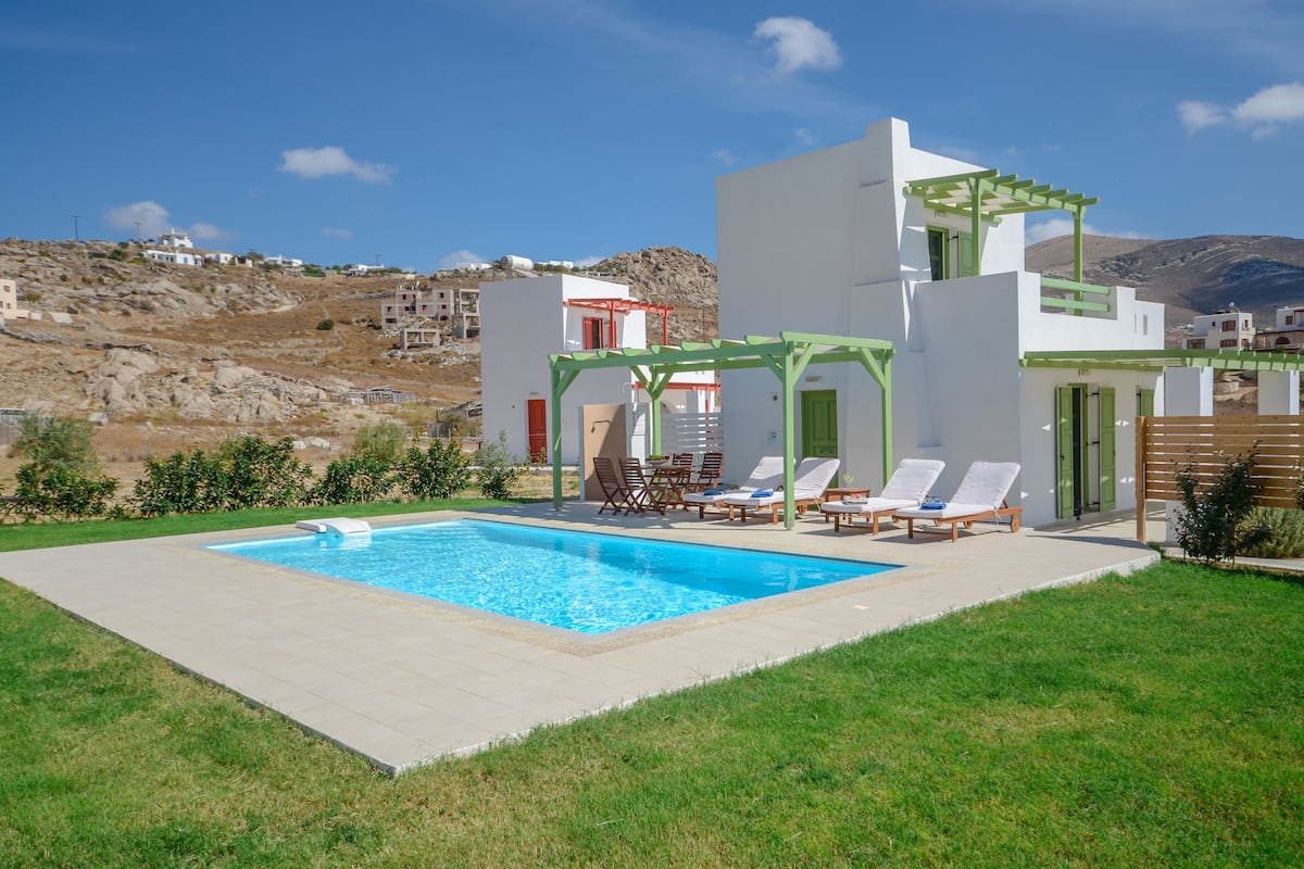A modern pool area with a clear blue pool, surrounded by a well-maintained lawn and a white building with a green door.