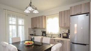 Una cocina moderna con armarios de madera, un refrigerador de acero inoxidable, una mesa de comedor con sillas blancas y una lámpara de araña.
