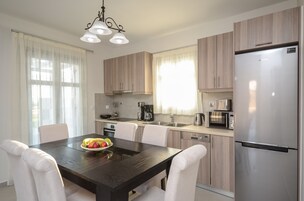 Una cocina moderna con armarios de madera, un refrigerador de acero inoxidable, una mesa de comedor con sillas blancas y una lámpara de araña.
