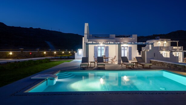 Una casa moderna con piscina, mobiliario exterior y un patio bien iluminado.