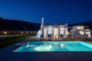 Una casa moderna con piscina, mobiliario exterior y un patio bien iluminado.