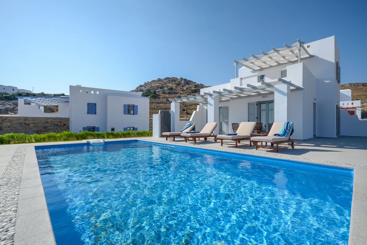 A modern pool area with clear blue water, white buildings, and a mountain in the background.
