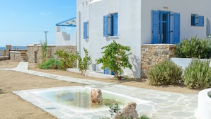 Un edificio blanco con contraventanas azules, un camino de piedra y una pequeña piscina.