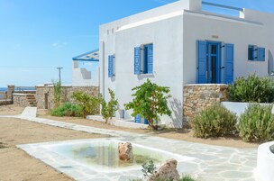 Un edificio blanco con contraventanas azules, un camino de piedra y una pequeña piscina.