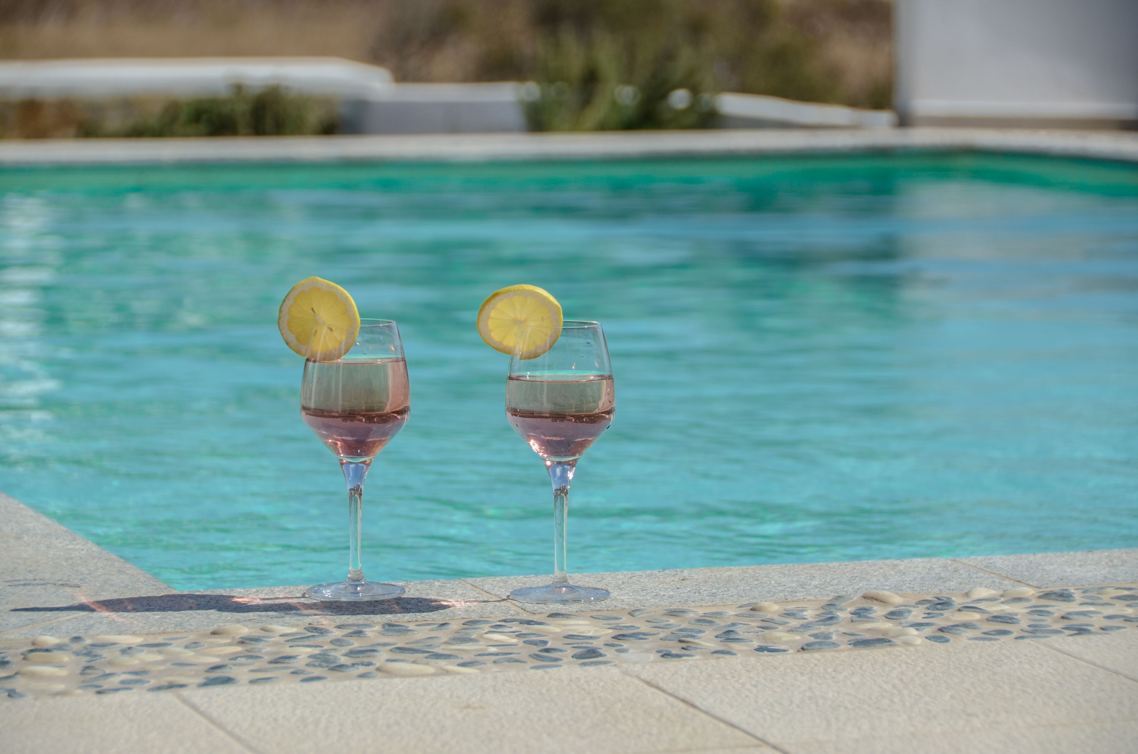 Zwei Gläser roter Wein mit Zitronenscheiben an einem gefliesten Poolrand.