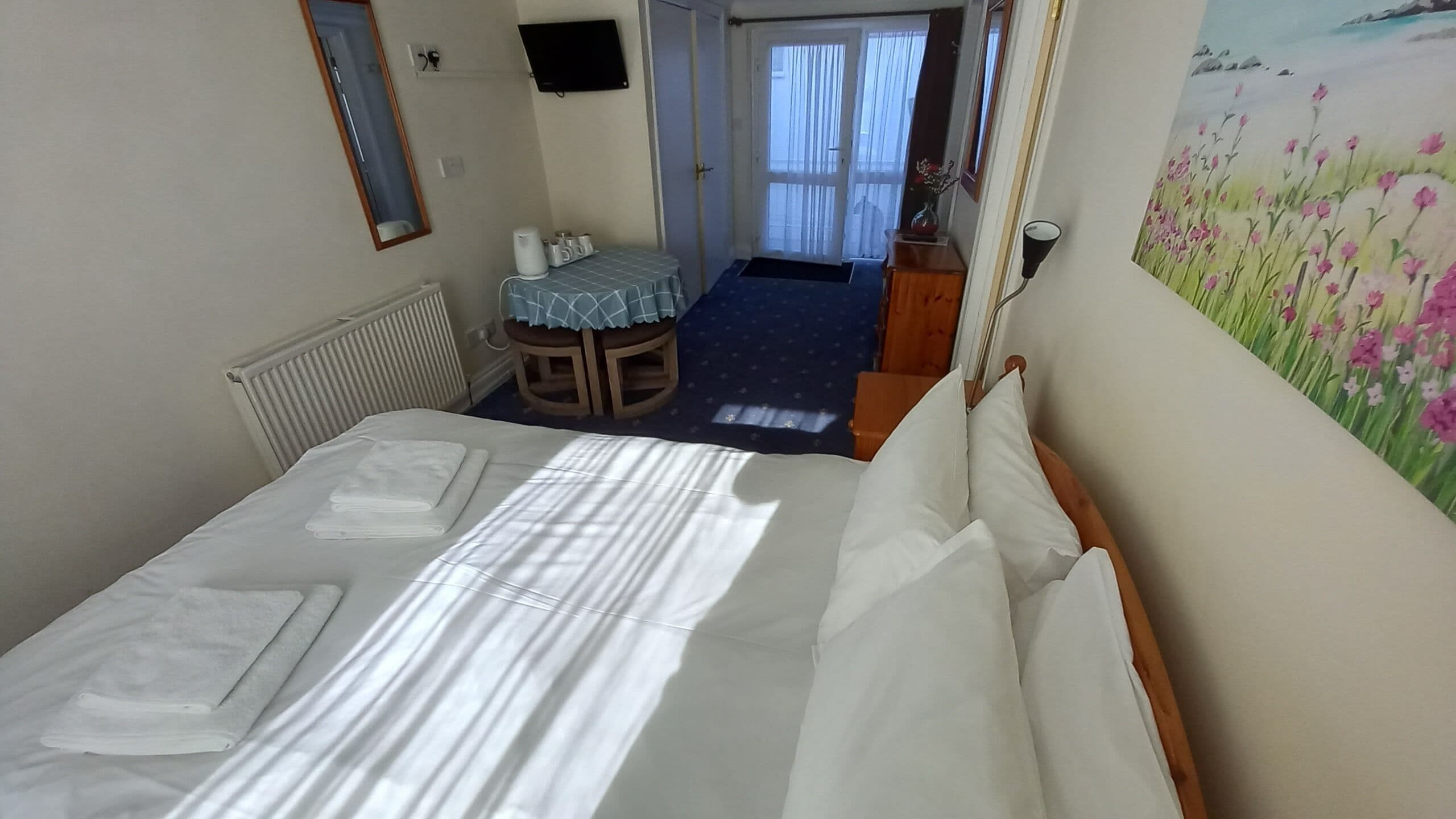Hotellihuone, jossa on sänky, pieni pöytä ja tuoli, patteri, televisio ja taulu seinällä.