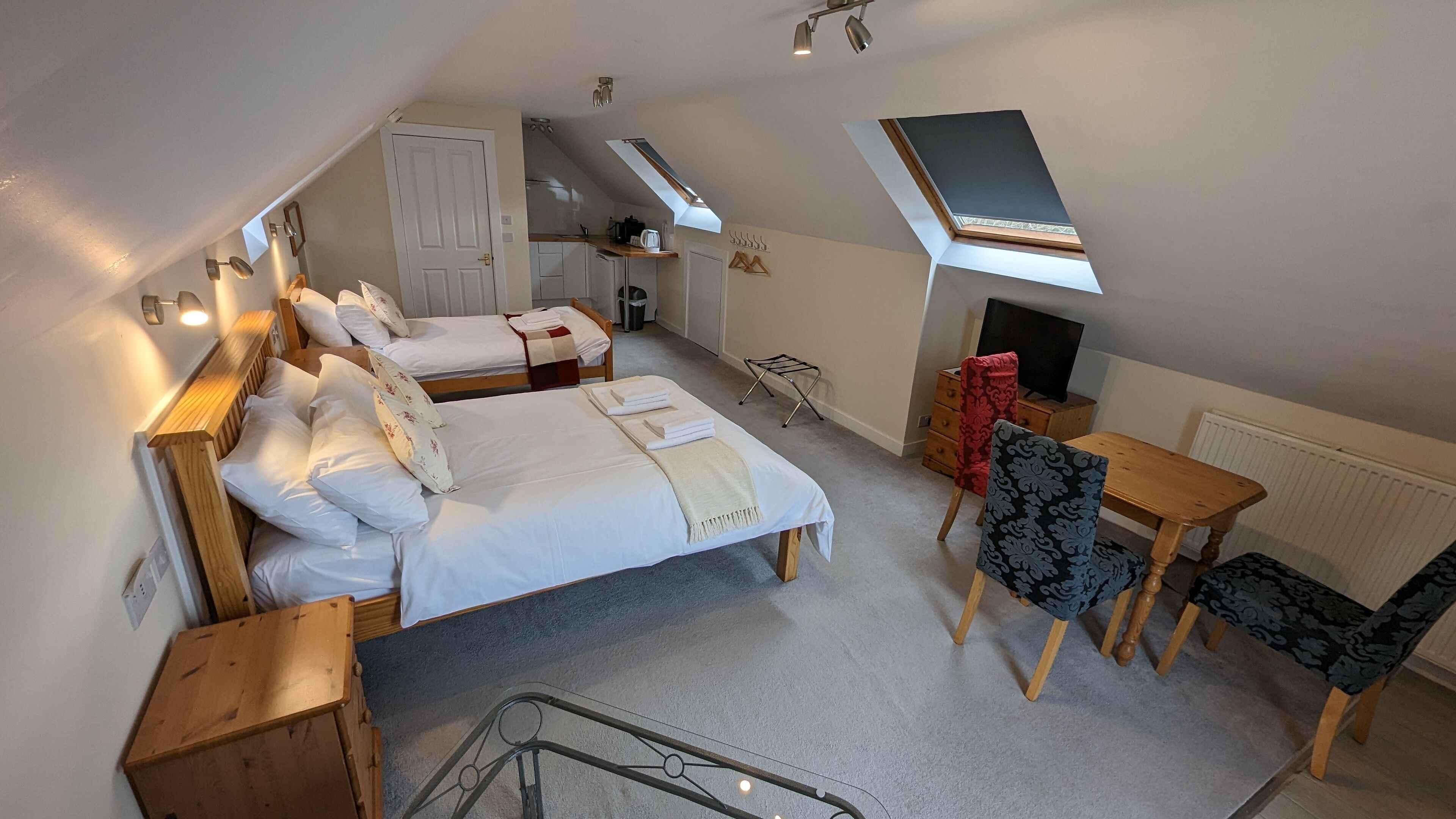 A bedroom with two beds, a desk, a chair, a radiator, and a skylight.