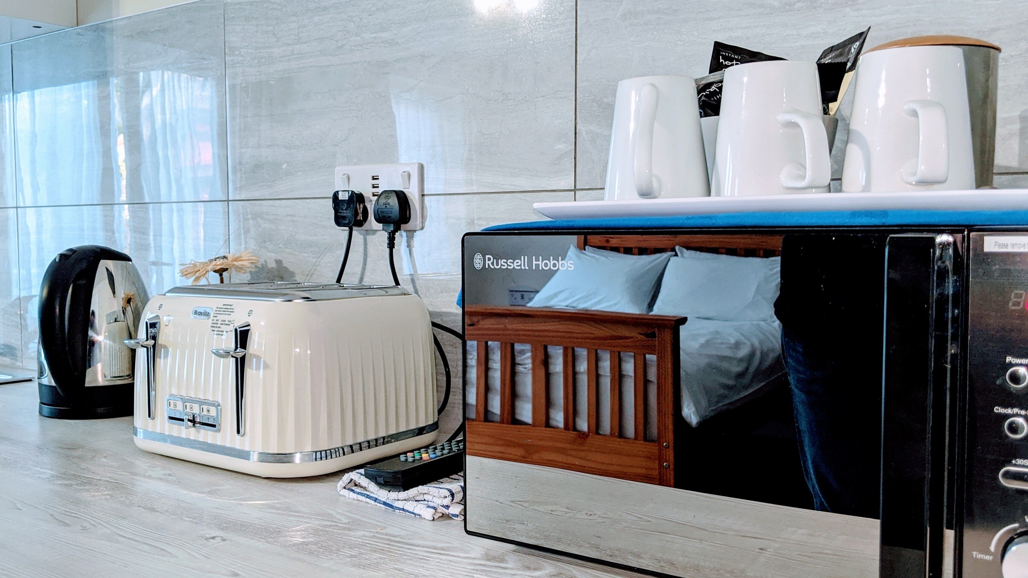 A modern kitchen with a toaster, a coffee maker, and a bed with a wooden headboard.