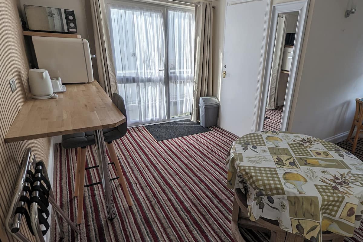 A hotel room with a wooden table, a bed with a patterned bedspread, a chair, and a view of the outdoors through a window.