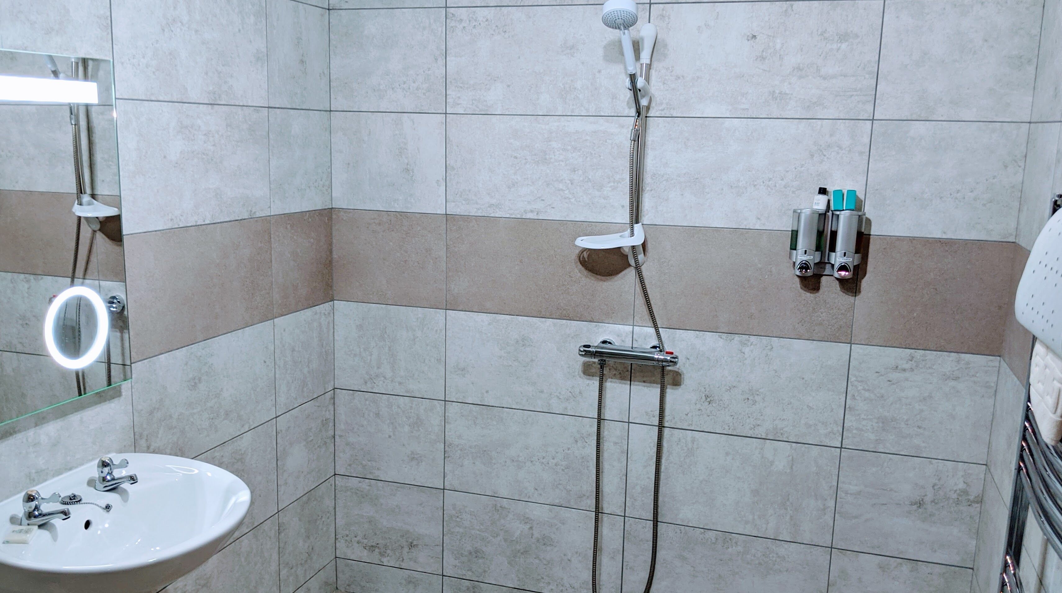 A bathroom with a sink, mirror, shower, and toiletries.