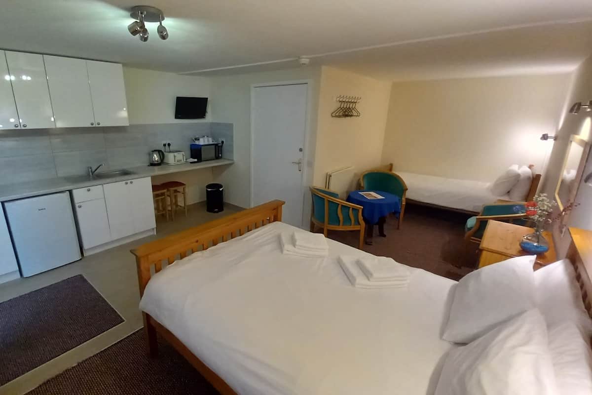 A compact hotel room with a kitchenette, a single bed, a small table, and a chair.