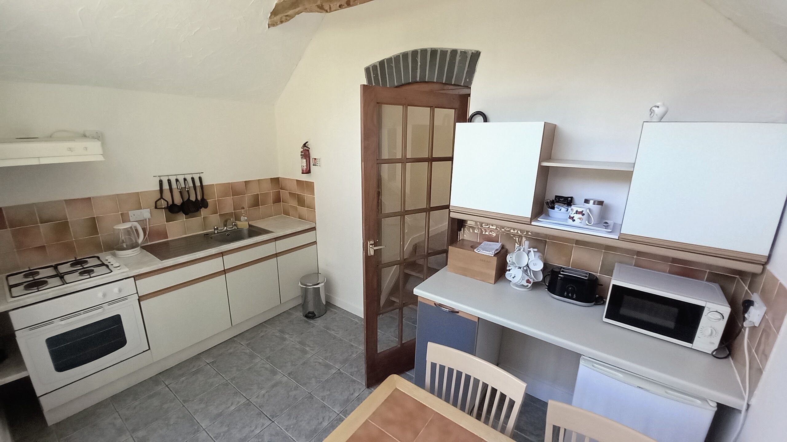 A compact kitchen with a gas stove, sink, and white cabinets. There is a microwave and a small table with chairs.