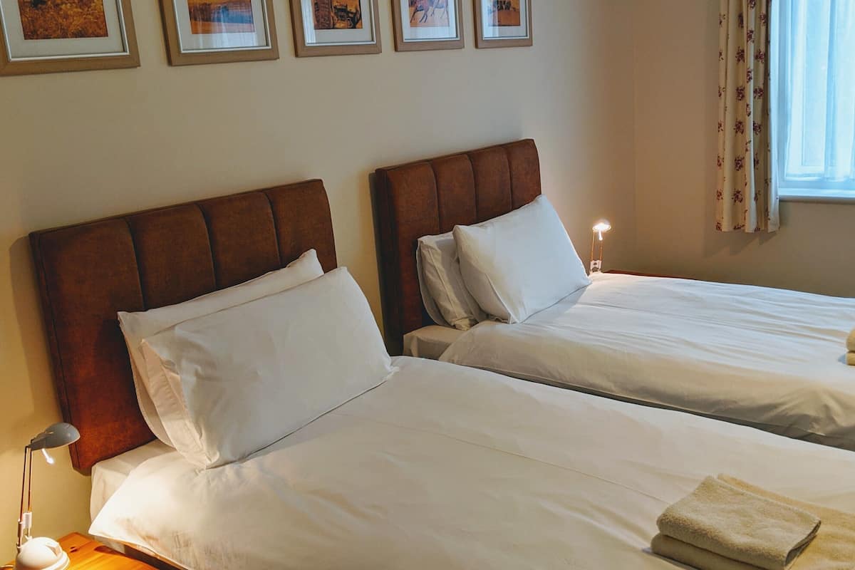 Two single beds with headboards, white bedding, and a window with curtains.