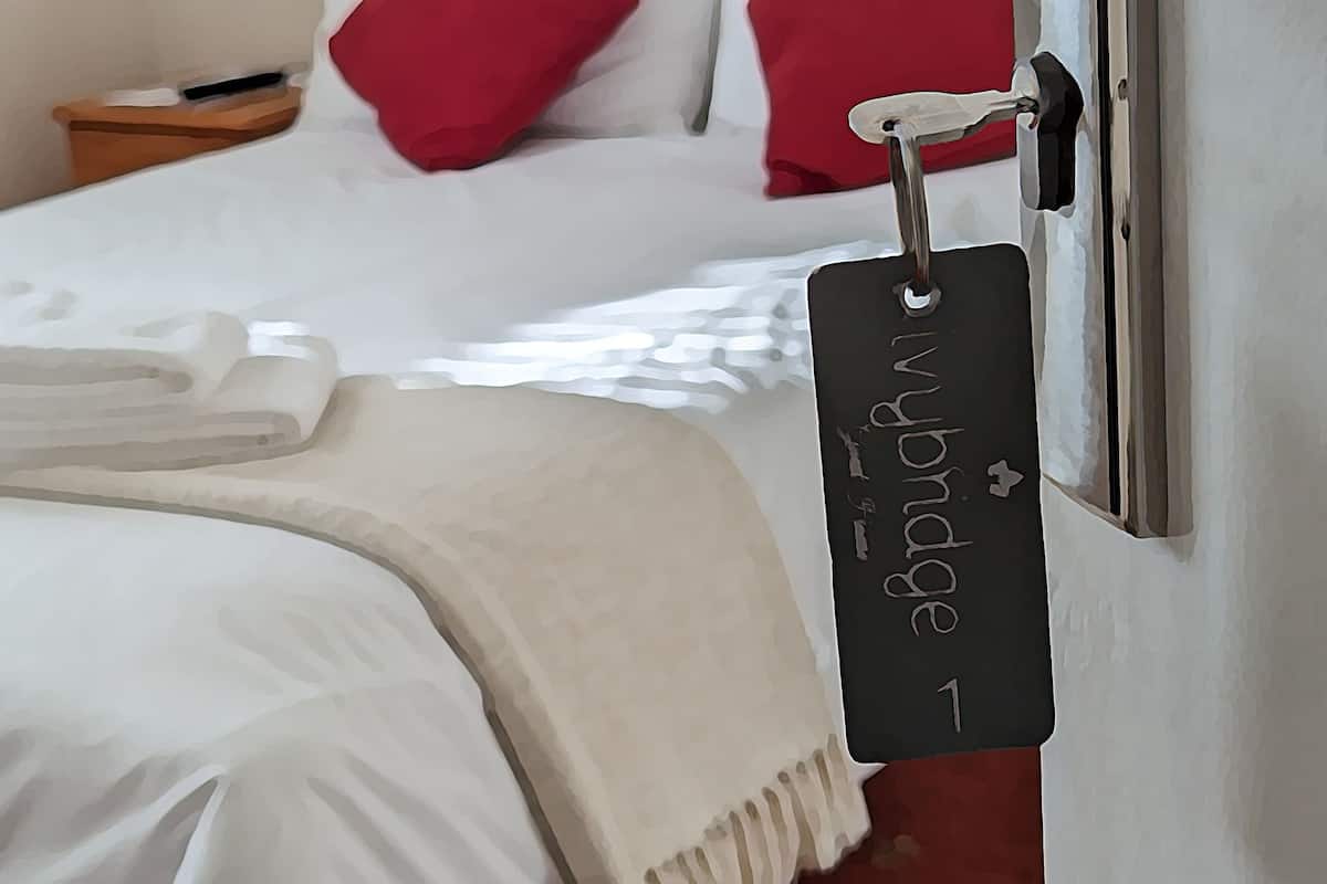 A neatly made bed with white linens, a red pillow, and a white towel on the side.