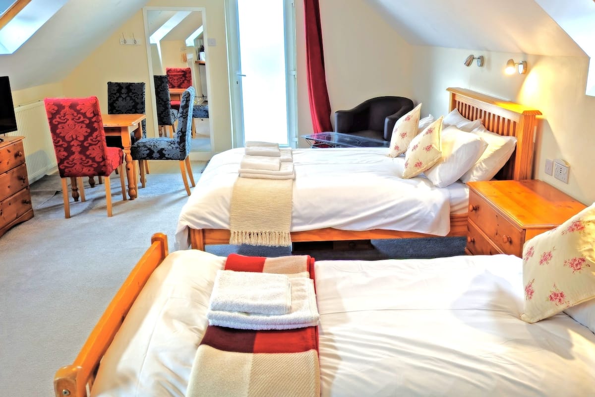 A cozy bedroom with two beds, a wooden nightstand, a chair, and a desk.