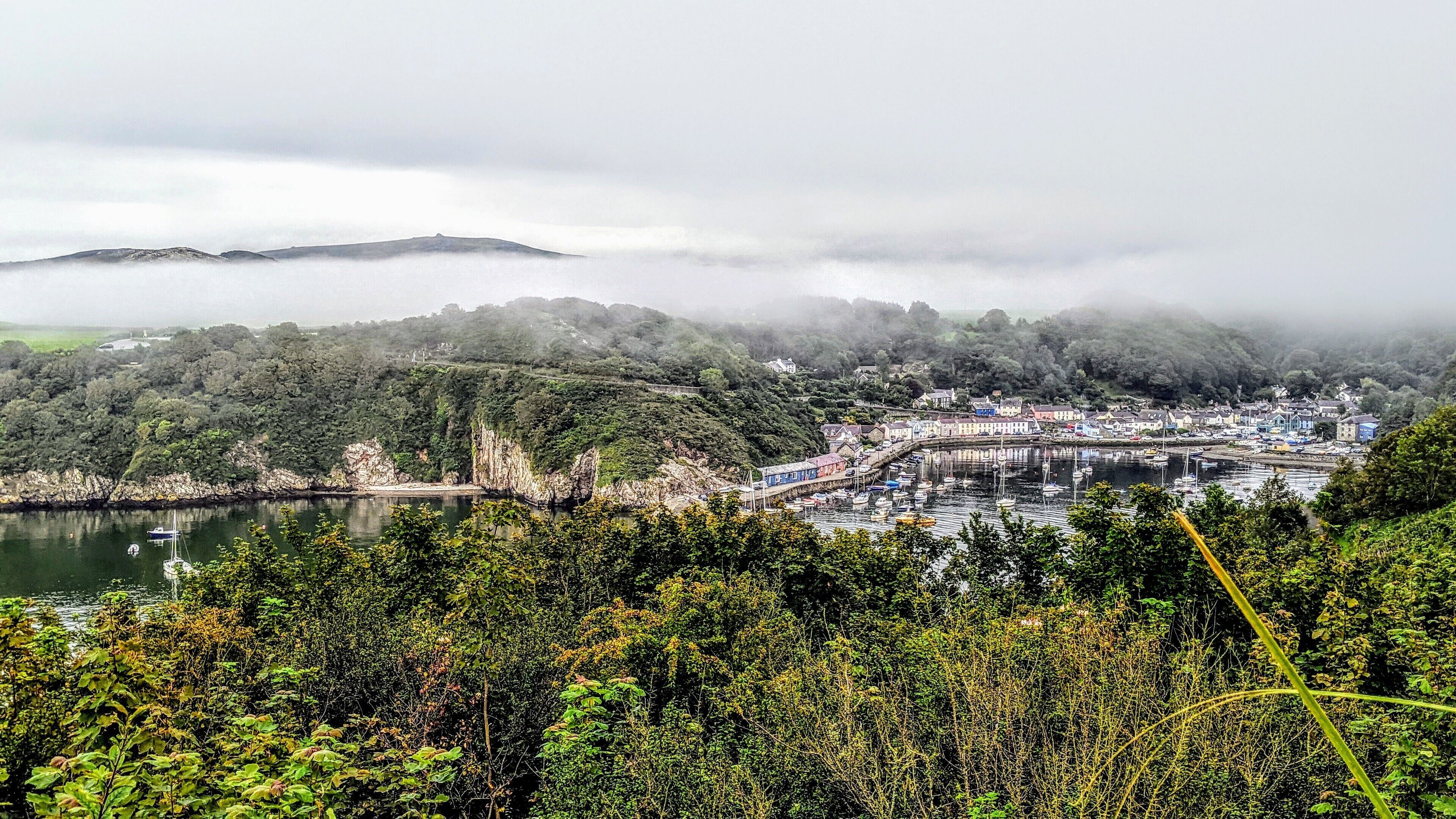 Un pueblo costero con un puerto deportivo, rodeado de exuberante vegetación y colinas.