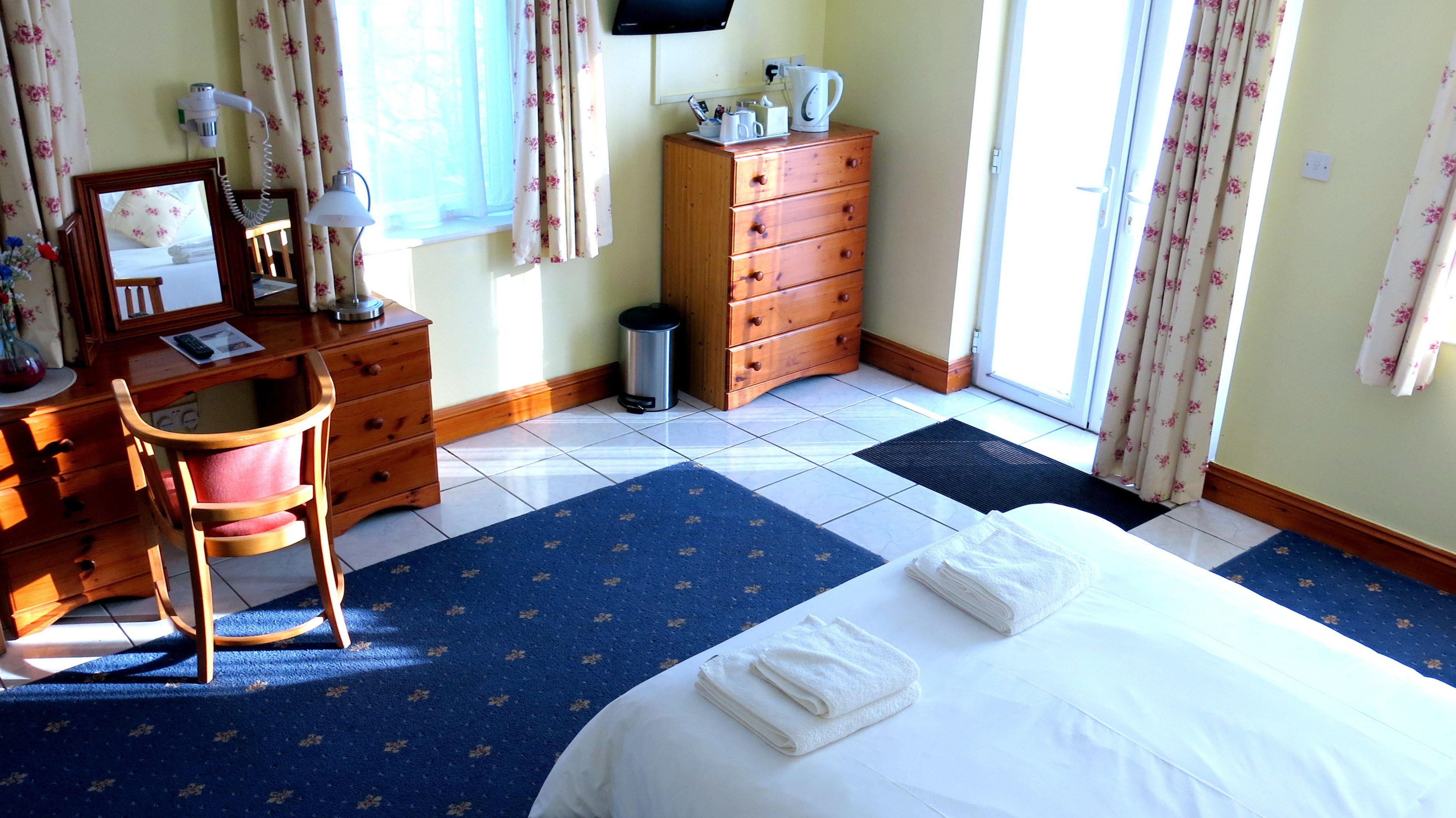 A hotel room with a bed, a desk, a chair, a dresser, a waste bin, and a window with curtains.