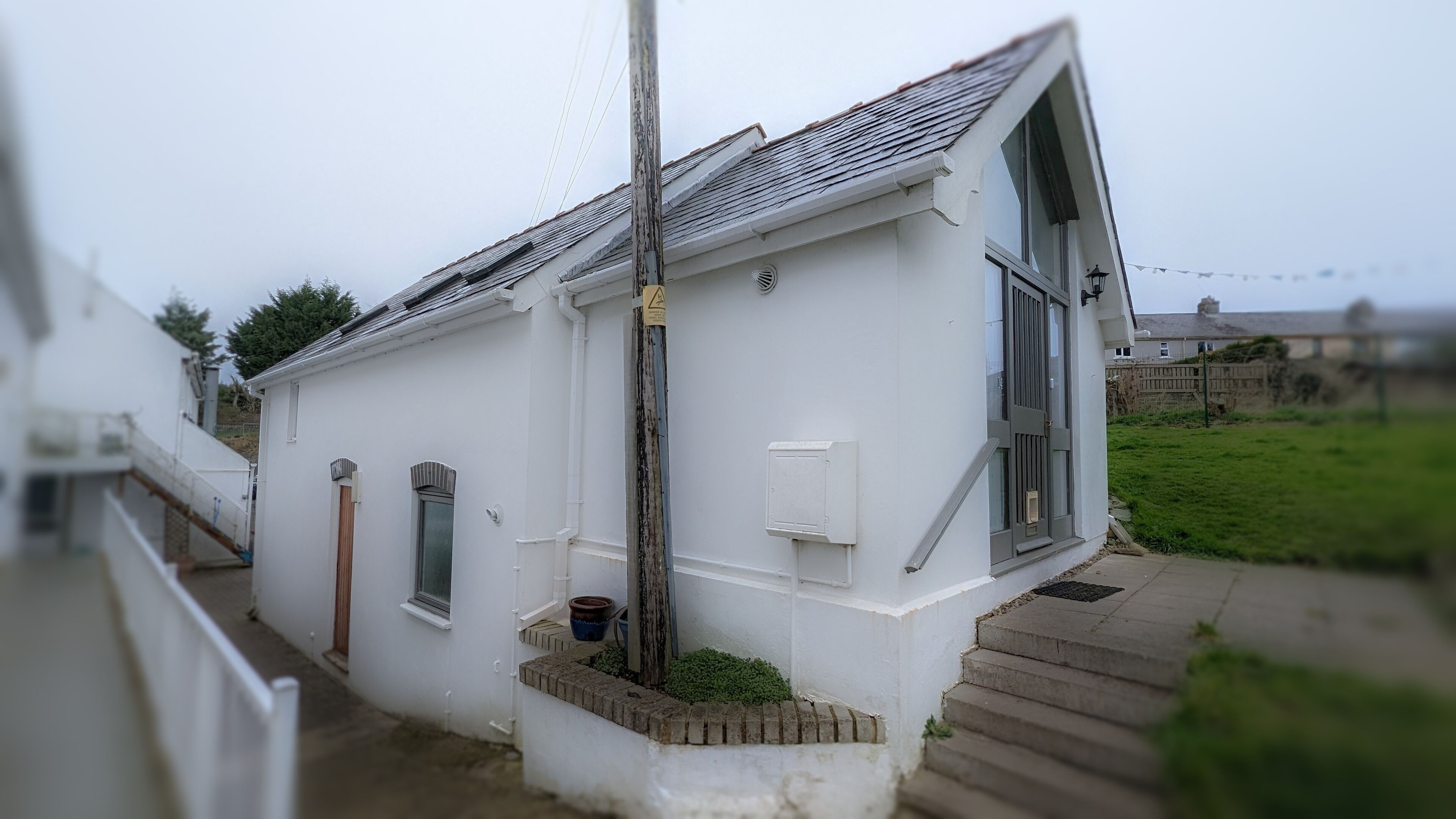 Un bâtiment blanc avec un toit en pente, un petit porche avec des marches et une fenêtre avec une porte.