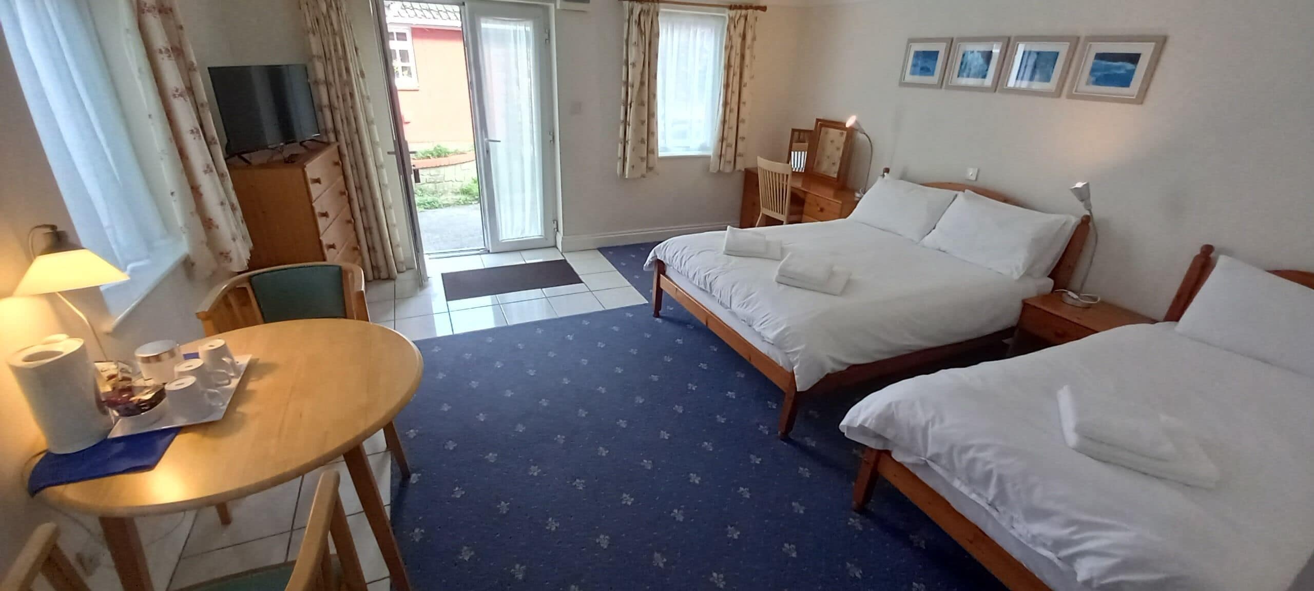 A hotel room with two beds, a desk with a chair, a TV, and a window with curtains.