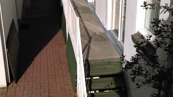 Un sendero estrecho que lleva a un edificio con múltiples ventanas y puertas, un camino de ladrillo y un banco verde.