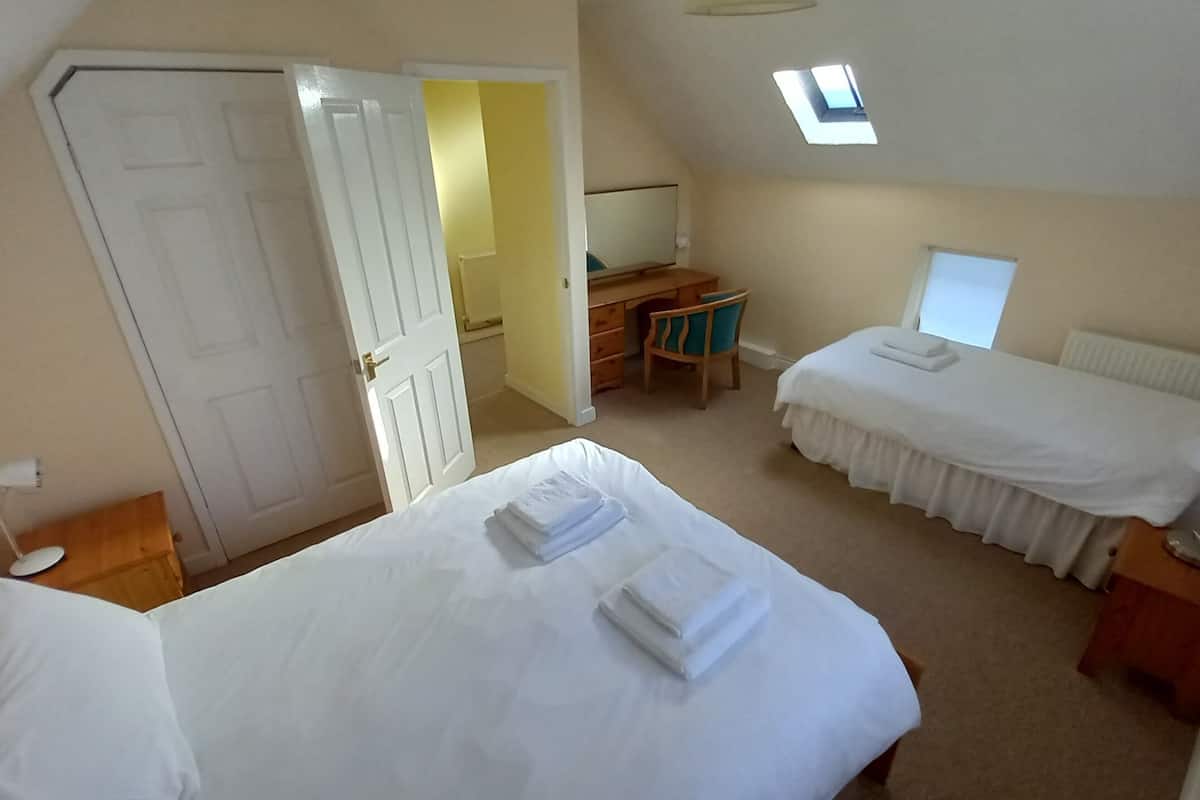 A hotel room with two beds, a desk, a chair, a small table, a lamp, and a window.