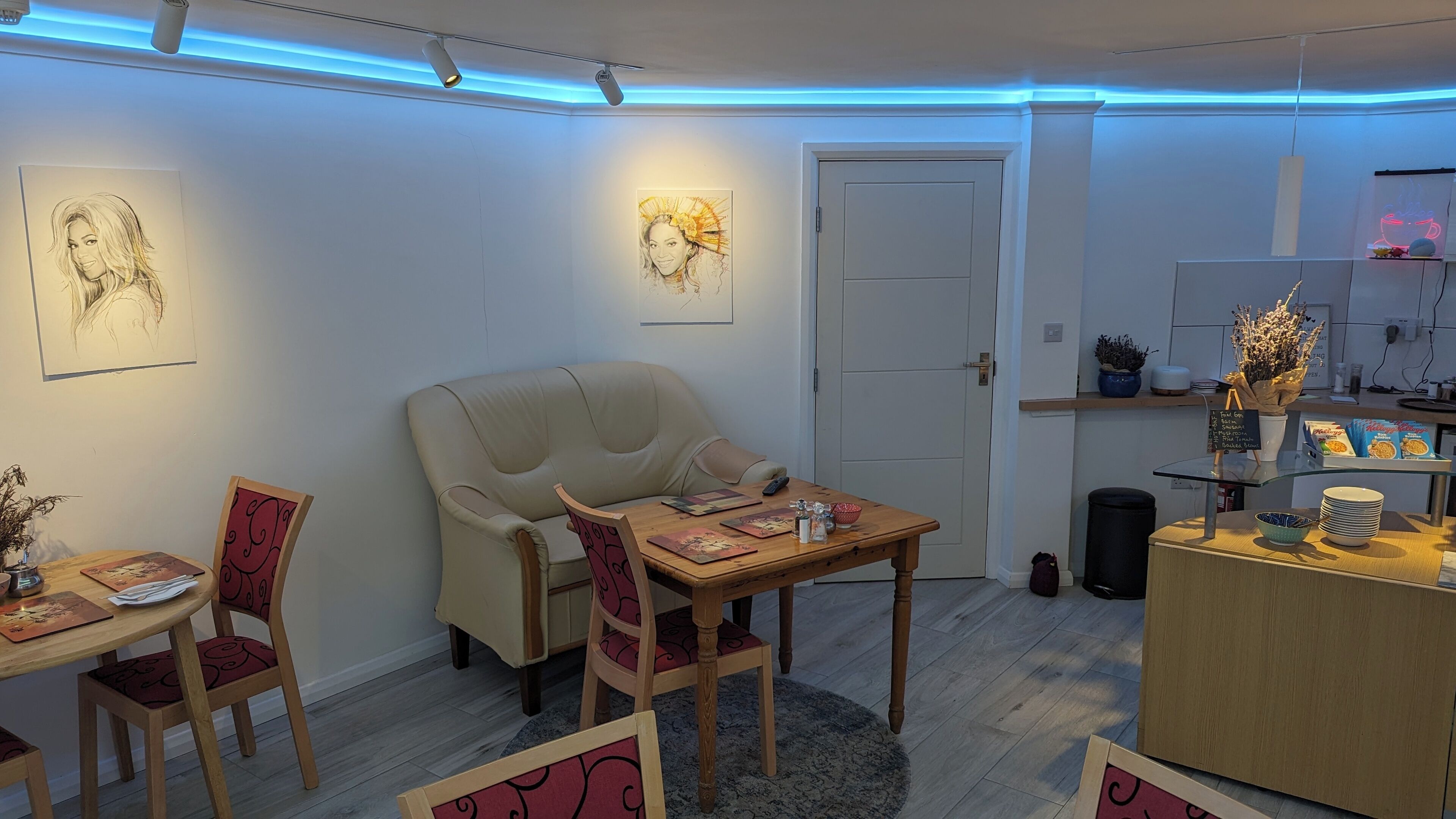 A cozy room with a dining table, chairs, a sofa, and artwork on the walls.