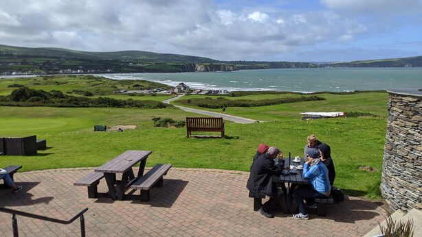 A coastal area with a stone wall, picnic tables, and a bench.