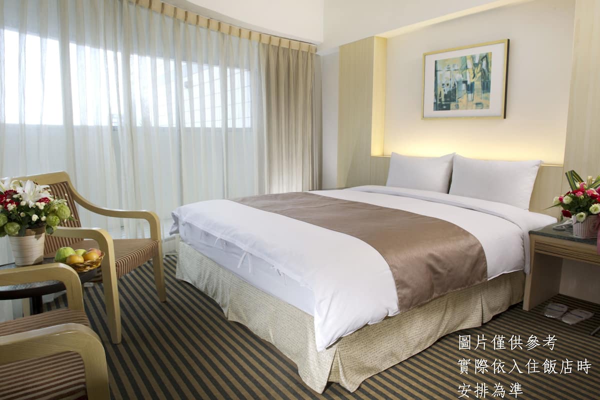 A hotel room with a large bed, a chair, a small table with a basket of fruit, and a vase of flowers.