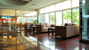 Um hall amplo com grandes janelas, uma mesa de centro de vidro e sofás listrados.