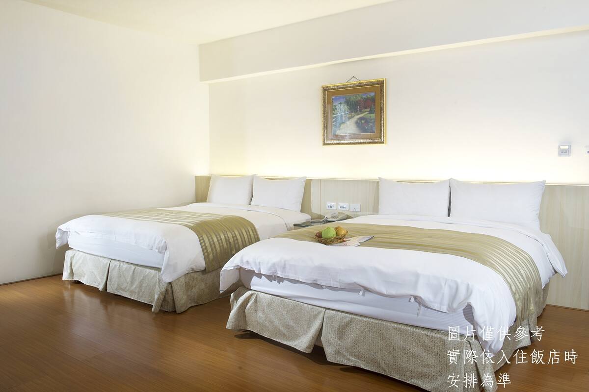 A hotel room with two beds, a painting on the wall, and a bedside table with a fruit basket.