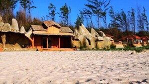 A sandy beach with traditional wooden structures and rock formations. - Doi Su Resort (Tan Thanh)