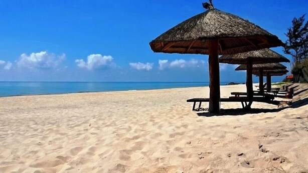 A beach with a thatched umbrella and wooden benches. - Doi Su Resort (Tan Thanh)