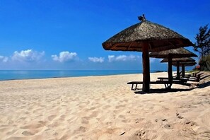 A beach with a thatched umbrella and wooden benches. - Doi Su Resort (Tan Thanh)