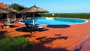 A swimming pool with lounge chairs and thatched umbrellas, surrounded by a tiled deck and greenery. - Doi Su Resort (Tan Thanh)