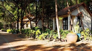 A pathway lined with trees and a building with a tiled roof and columns. - Doi Su Resort (Tan Thanh)