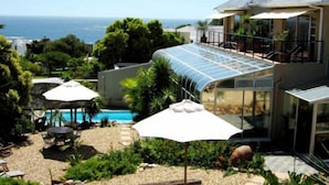 A modern house with a glass conservatory, a pool, and a view of the ocean. - Villa Surprise (Cape Town)