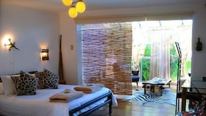 A bedroom with a bed, a zebra-patterned rug, a small table, and a view of greenery outside. - Villa Surprise (Cape Town)