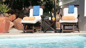 Two lounge chairs by a pool with towels and a bottle of wine. - Villa Surprise (Cape Town)