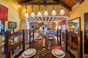 Un espace repas avec une longue table dressée pour un repas, des chaises en bois, des lampes suspendues et un escalier en arrière-plan.