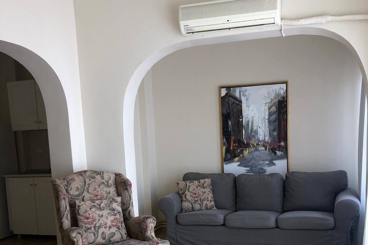 A living room with a floral armchair, a grey sofa, and a painting on the wall.