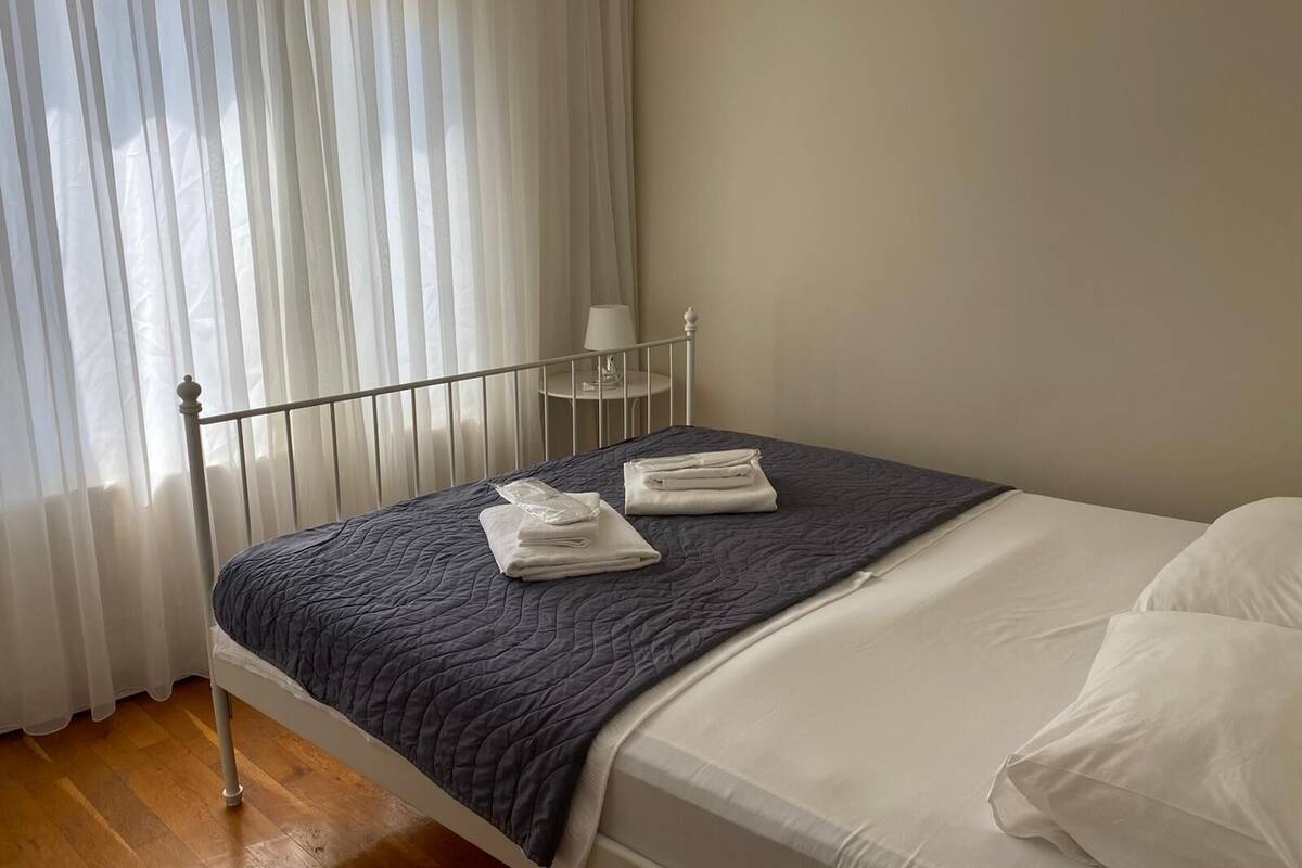 A neatly made bed with a dark quilt, white pillows, and folded towels.