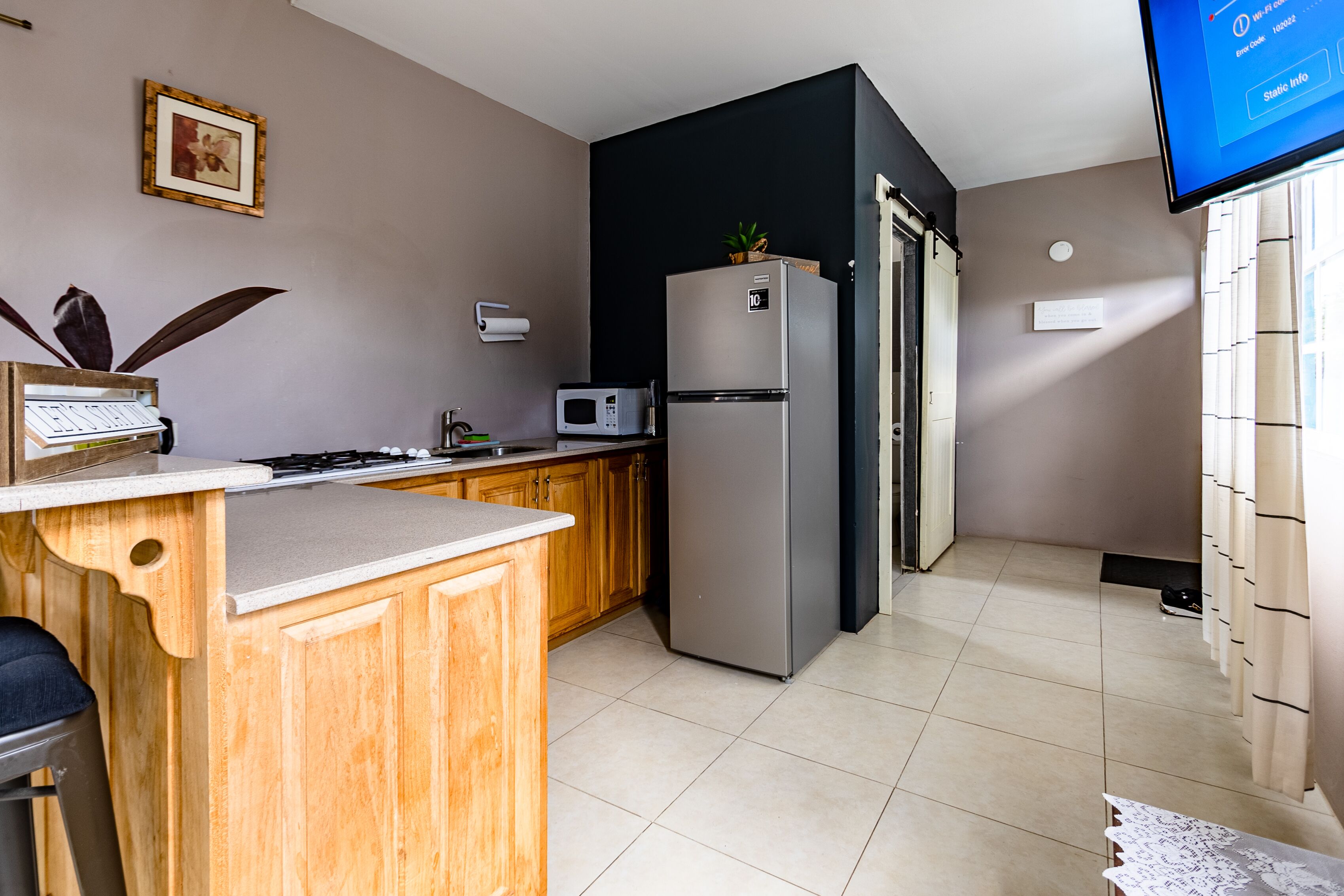A modern kitchen with wooden cabinets, a stainless steel refrigerator, a microwave, and a small island with a sink.