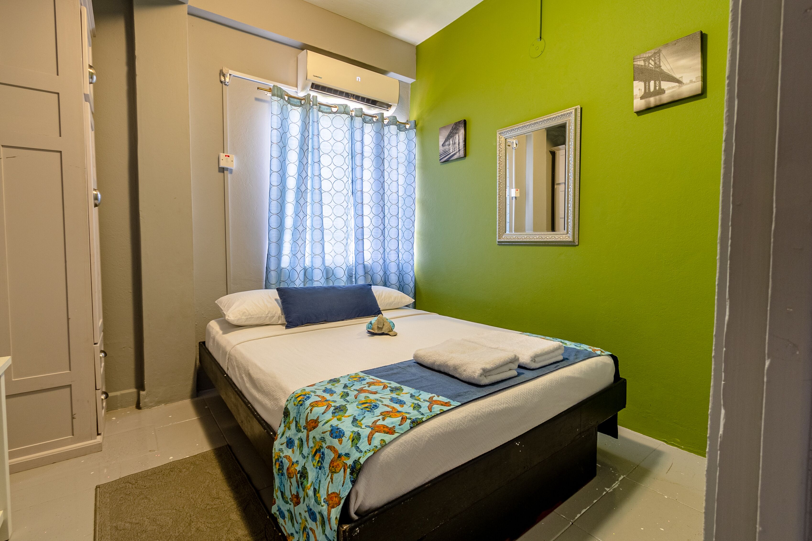A bedroom with a bed, a window with curtains, a mirror, and a green wall.