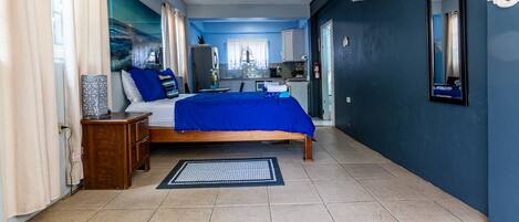 A bedroom with a bed, bedside table, and a view of the kitchen.