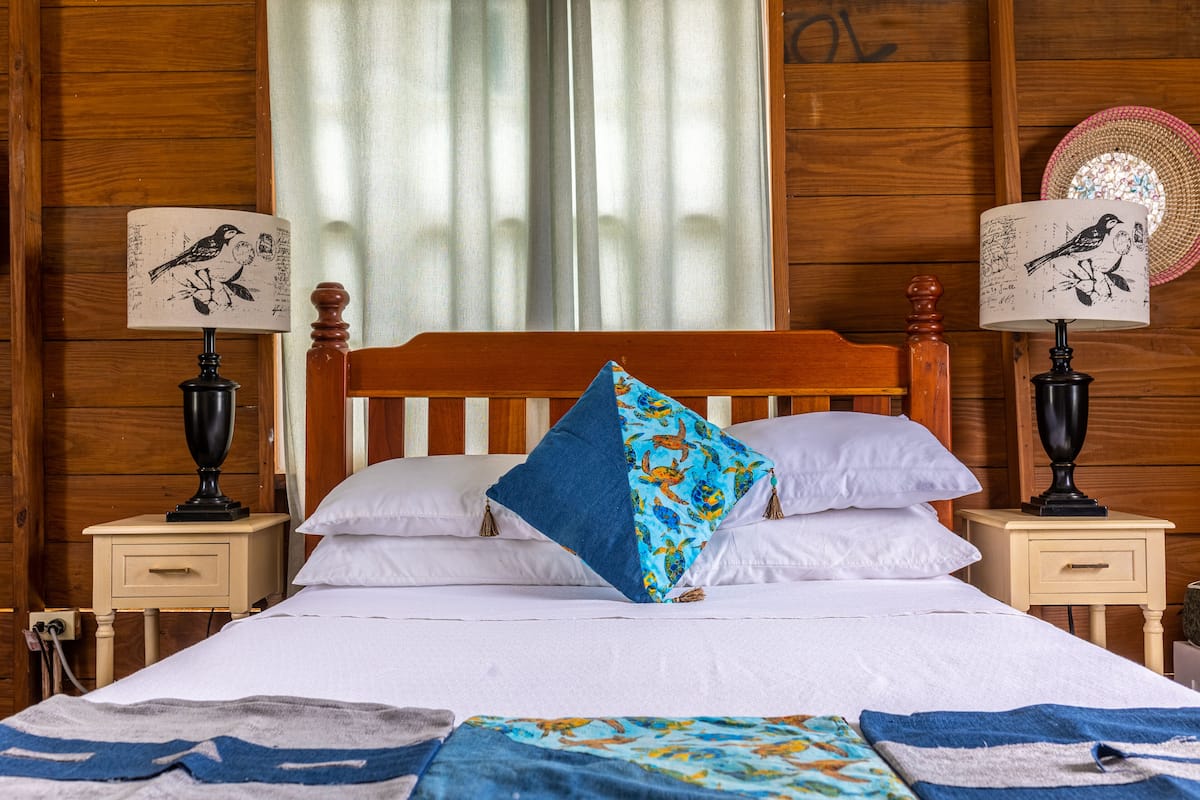 A wooden-paneled room with a bed, two bedside tables with lamps, and a window with curtains.