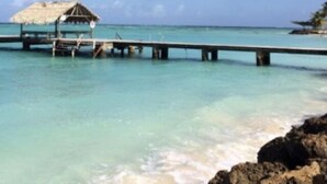 A pier extending into a clear blue sea with a thatched-roof structure at the end.