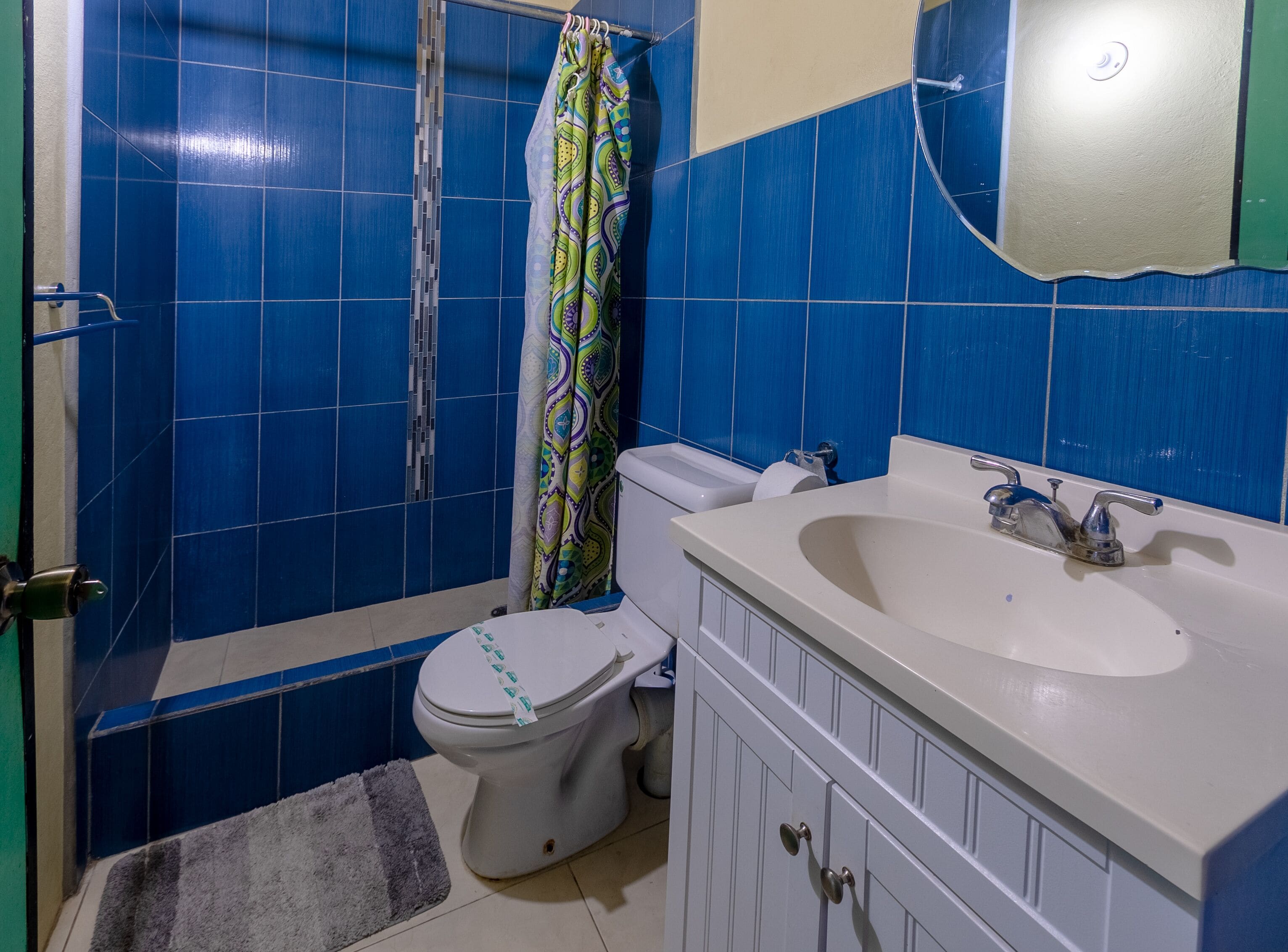 A bathroom with blue tiles, a toilet, a shower curtain, a sink, and a mirror.