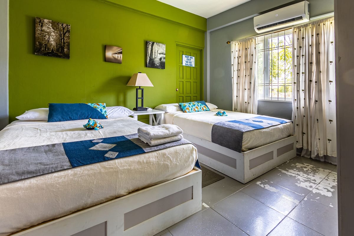 A hotel room with two beds, a nightstand, a lamp, and artwork on the walls.