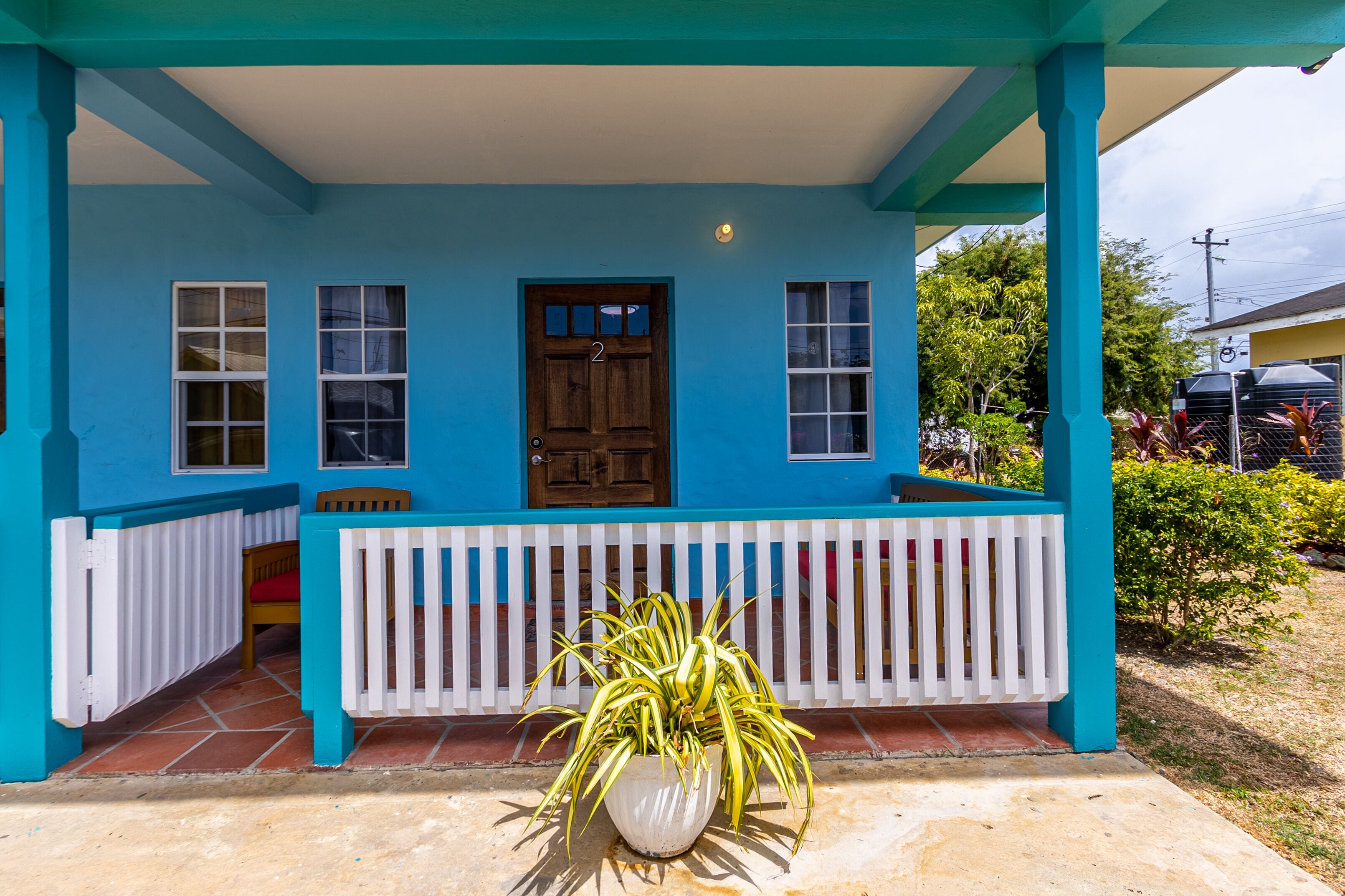 A blue building with a wooden door, white railings, and a potted plant in front.