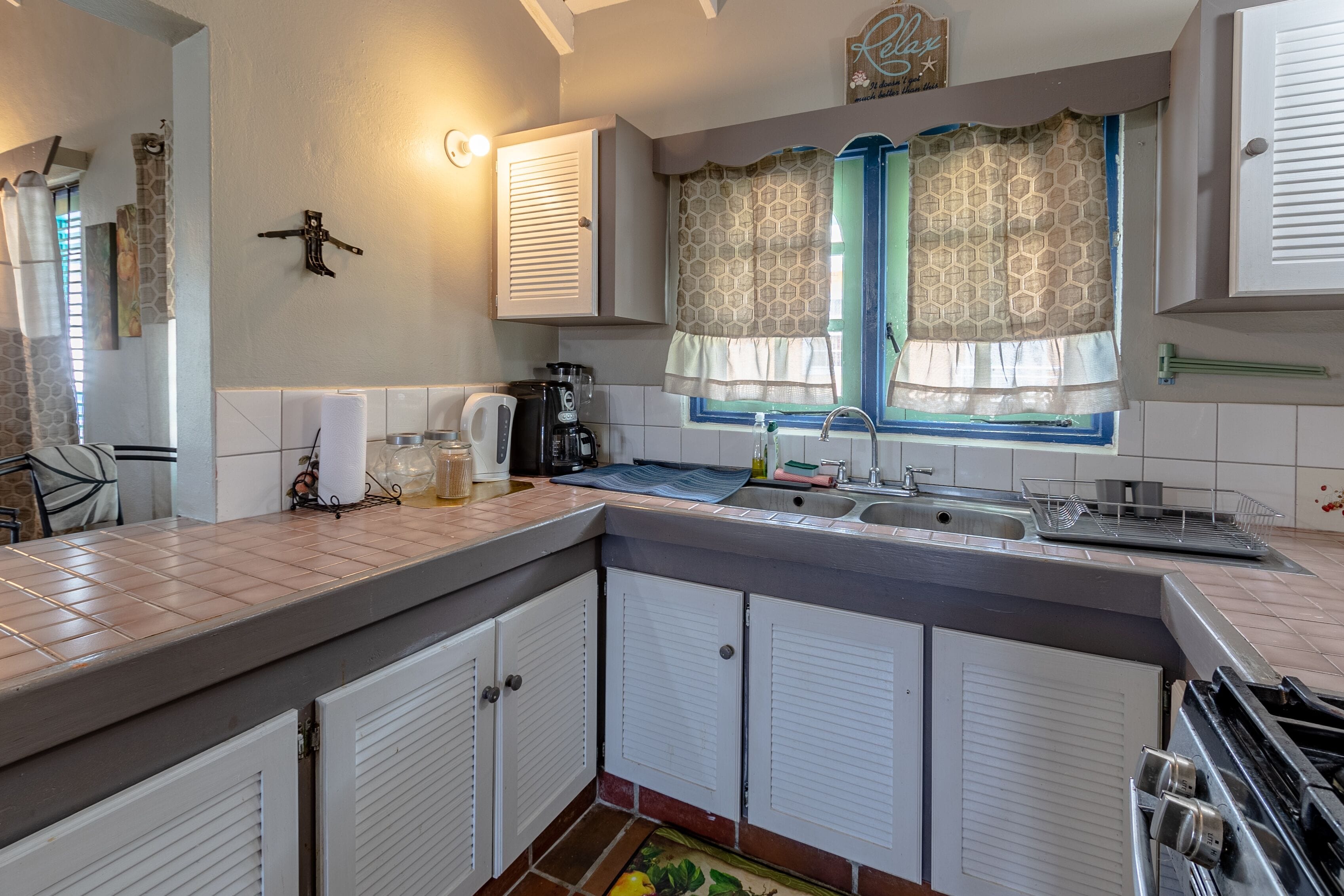 Una cocina con una isla grande, armarios blancos, una estufa empotrada y una ventana con cortinas estampadas.